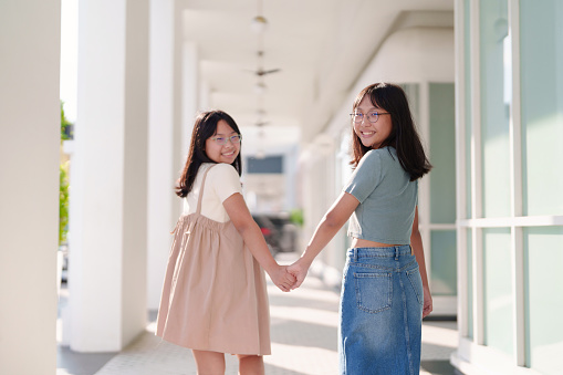 Two cheerful young Asian siblings look back with beautiful smiles while joyfully exploring Georgetown, Penang.