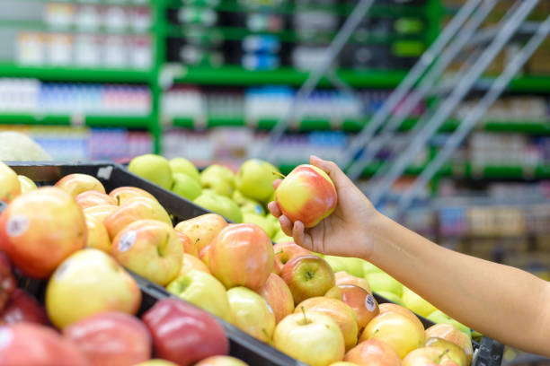 istock Hand holding an apple at a supermarket. 2111491301