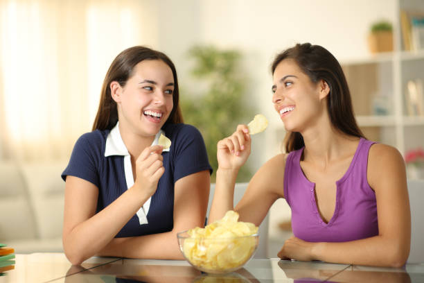 istock Two happy friends talking eating potato chips 2111492330