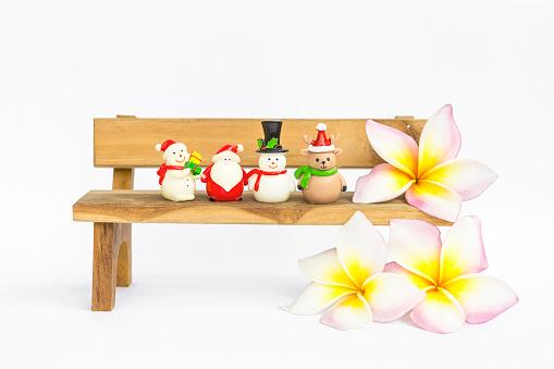 Christmas doll collections on wooden bench with plumeria flower on white background, Christmas decoration item, festive and holiday concept