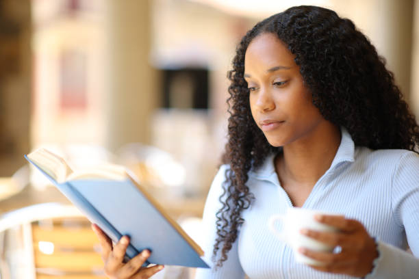 istock Black woman reading a paper book drinking coffee 2111494445