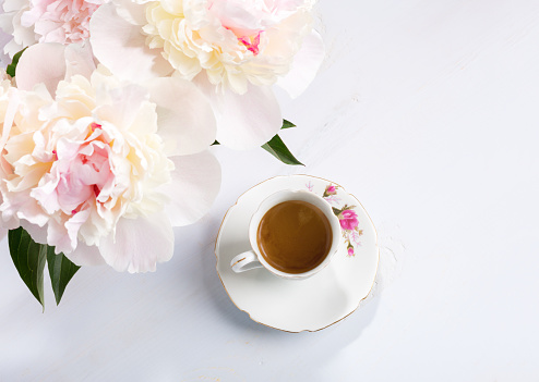 Small bouquet of peonies  and old porcelain cup with coffee  on a light lilac wooden table. Flat lay