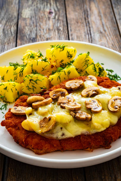 istock Breaded seared chicken cutlet with cheese, white mushrooms and boiled potatoes on wooden table 2111502302