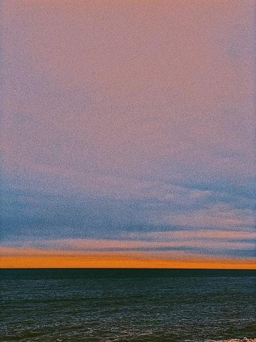 Brighton Beach, East Sussex – March 16, 2024: Sunset over the sea, with dark blue clouds contrasting vibrant orange, pink, and purple hues in the sky. The sun's warm rays reflect shimmering on the dark water's surface.