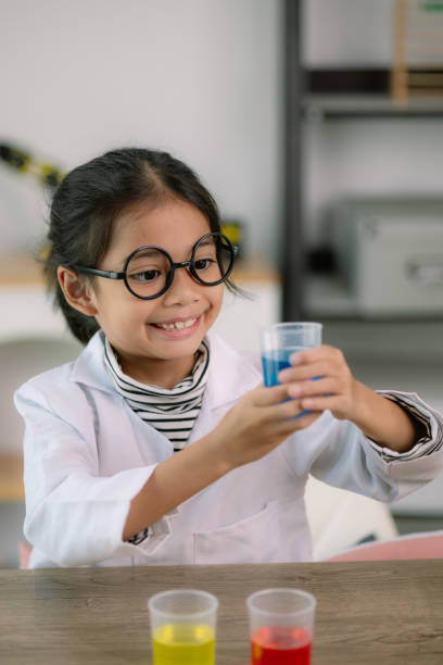 istock Little cute girl with a microscope holding a laboratory bottle with water experiment study scientists at school. Education science concept. 2111521660
