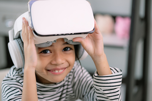 Cute Asian little girl wearing VR glasses with a laptop placed on the table in STEM technology class. Online education. Erudition.