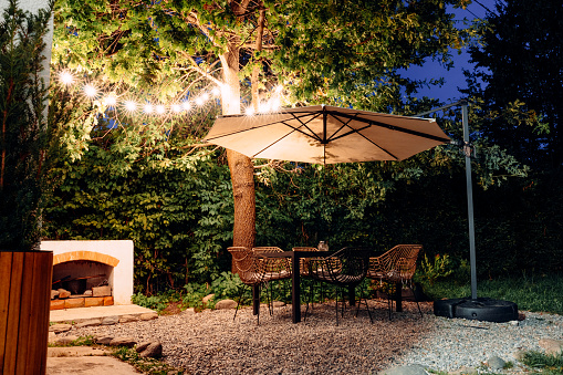 An outdoor patio with table, chairs, and umbrella illuminated by string lights