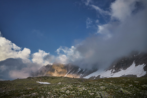 Sunlight breaks through clouds onto a mountain, above a green, rocky slope, creating a dramatic scene