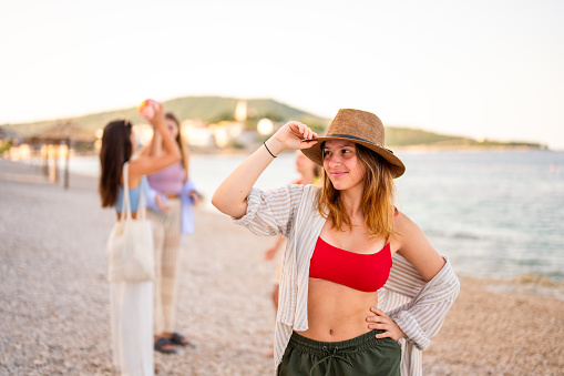 Portrait of a teenage girl with a straw hat on the beach with some friends in the blurred background.