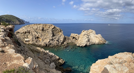 Summer morning on Sant Josep de sa Talaia beach in Ibiza, Spain. Beautiful sea views up a cliff. Crystal clear sea water. Turquoise waters in hidden bay. Deserted beach.