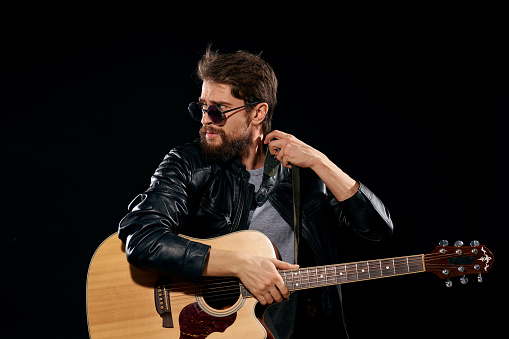 A man with a guitar in his hands leather jacket performed on a black background. High quality photo