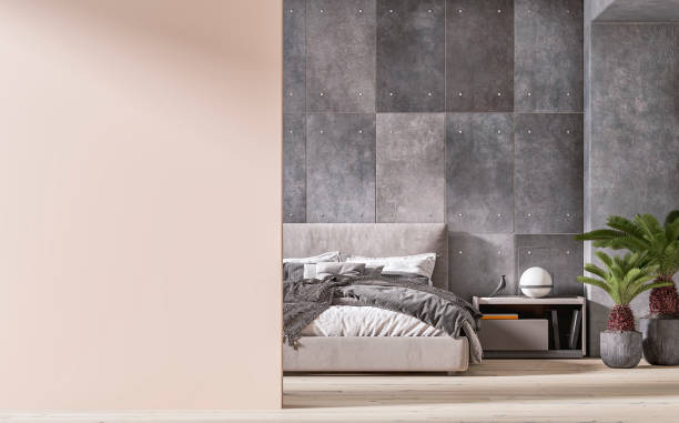 istock Modern bedroom interior: an empty blank pale blush pink wall  in foreground, a room with a grey textile double bed in front of a concrete tiled wall and niche with decoration in the background 2111604971