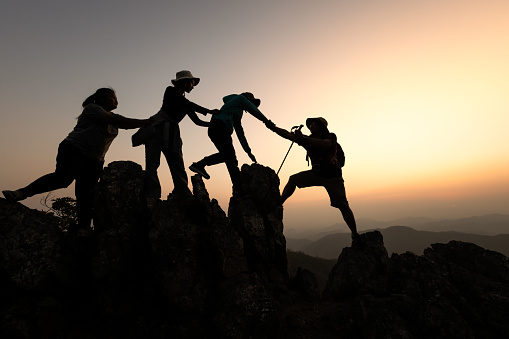 Silhouette of hikers climbing up on the mountain,team work and helping concept. Climber success.
