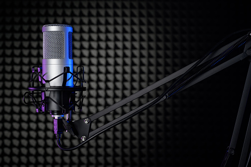 Professional silver microphone in the sound recording studio with black soundproof foam panel.