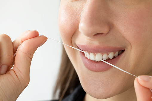 Woman with beautiful smile using floss for teeth