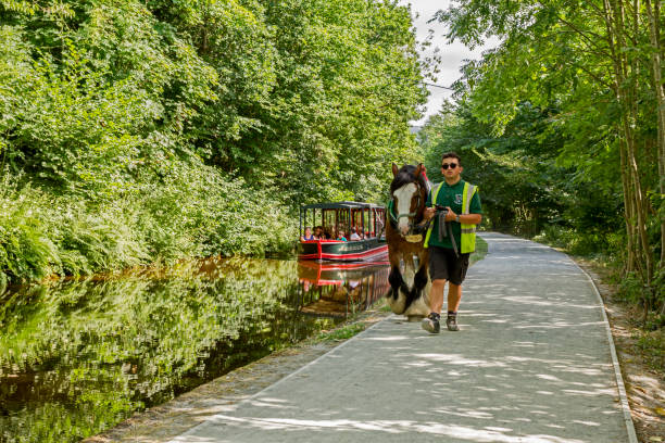 View of a horse drawn boat in Llangollen, UK.  A man can be seen with the boat and people can be seen on the boat.