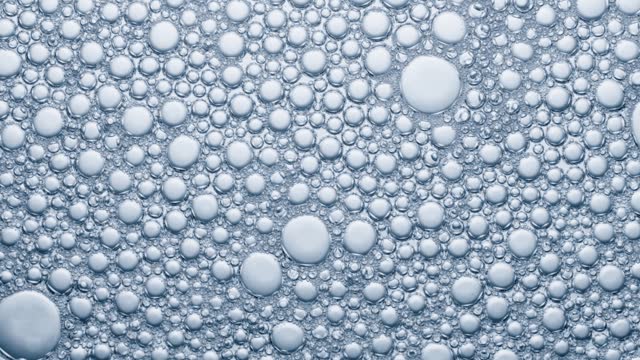 Multitude of air bubbles in a soap solution, bubbles burst on contact with air.