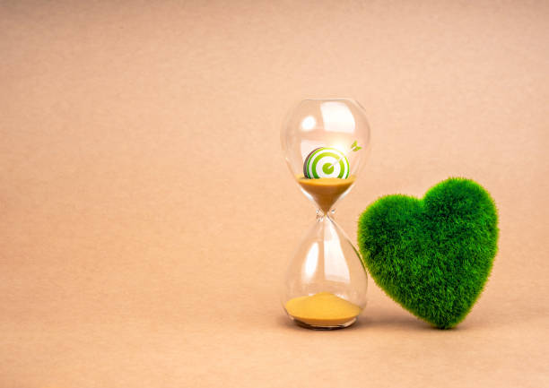 Environment sustainability, time and responsibility concept. Target of restoring our earth. 3d green target icon in hourglass and green grass heart shaped on recycle paper background with cop space.