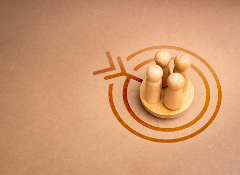 Stakeholder, business connection, teamwork, and team building concept. Four wooden figures as businessman standing together on round podium and target icon on brown recycle background with copy space.