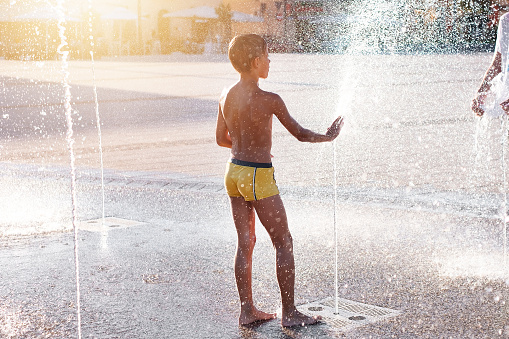 Children in the city in summer in abnormally hot weather splash and have fun in the stone fountain. Boy play in spray of water.
