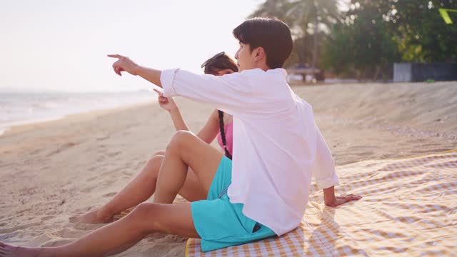 Asian young couple having picnic on the beach during summer together. Attractive romantic man and woman feeling happy and relax enjoy holiday vacation trip for honeymoon in the tropical sea island.