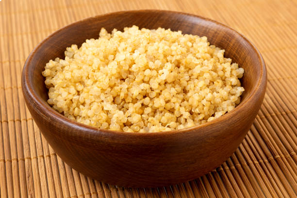 istock Cooked white quinoa in a dark wood bowl isolated on bamboo matt. 2111738980