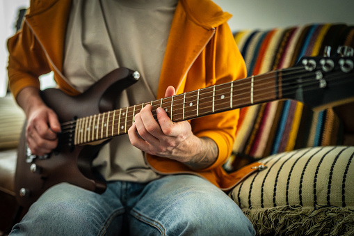 Mid section of man learning to play guitar while sitting on sofa at home.