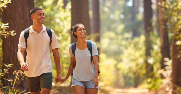 istock Young Couple Holding Hands Wearing Backpacks Hiking Along Trail Through Countryside 2111750607