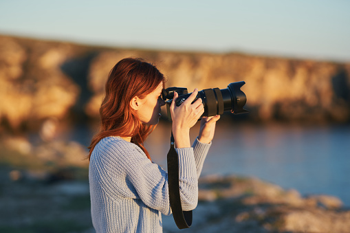 woman with a camera at sunset in the mountains in nature near the sea. High quality photo