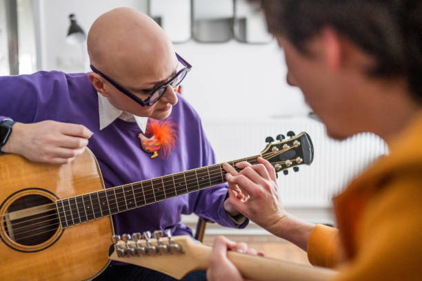 Young man teaching woman to play guitar while sitting on sofa during music lesson at home.