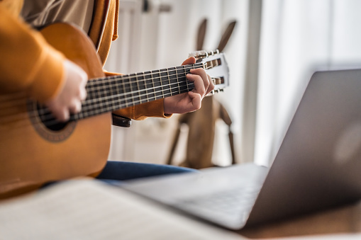 Close-up of girl learning to play guitar of online lesson on laptop at home.