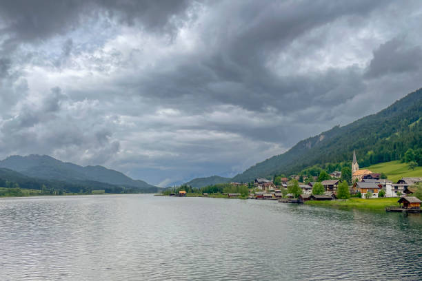 View on Techendorf village on the shore of the Weissensee or Weißensee lake in Carinthia in Austria within the Gailtal Alps mountain range during an overcast springtime day.