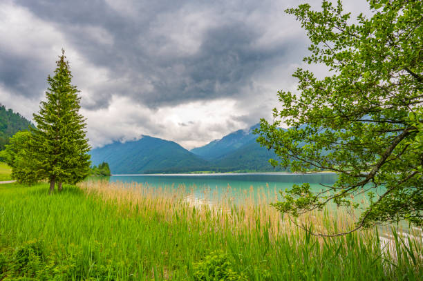 Scenic wide-angle long exposure view of Lake Wolfgang (Wolfgangsee) surrounded by snow-dusted Salzkammergut mountains during a dramatic cloudy sunrise in Austria