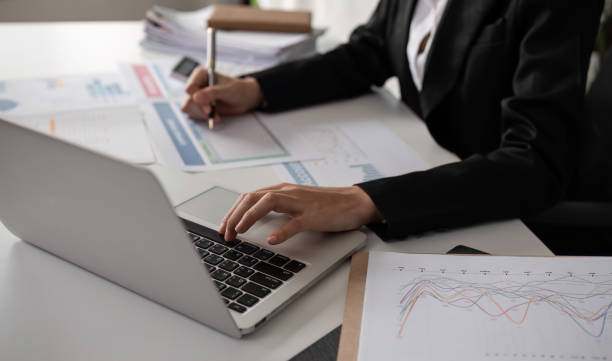 istock Close up, A young accountant calculates financial figures and company spending graphs using a calculator and laptop to take notes. 2111794189