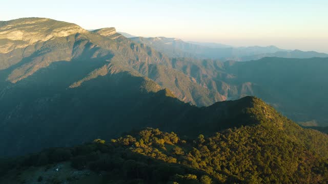 Gorgeous aerial view over a crest covered with trees at the top of a mountain range after sunrise, drone footage