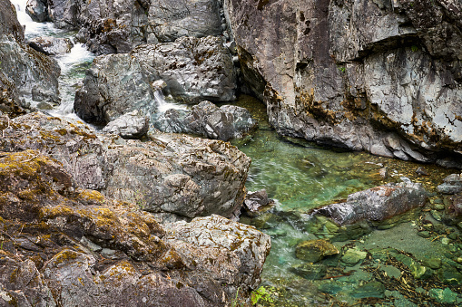 A small creek rushing between steep rocks to a bright green pool of water