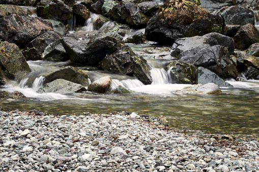 A stream running over lichen covered rocks and boulders creating small waterfalls on its way to the gravel creek bed.