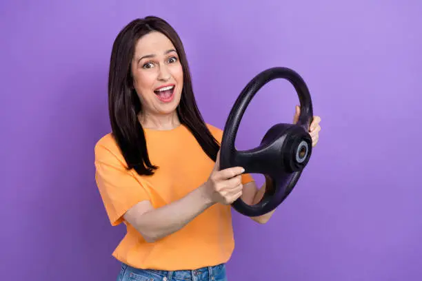 Photo of Photo of overjoyed brunette hair funny woman in yellow t shirt drive new volkswagen auto fast speed isolated on violet color background