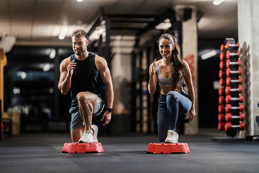 A muscular couple in shape is exercising gluteus and legs in a gym.
