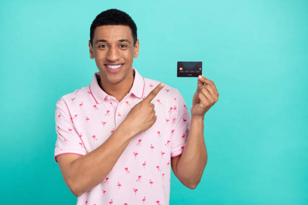 istock Portrait of handsome guy beaming smile indicate finger arm hold debit card empty space isolated on turquoise color background 2111852626