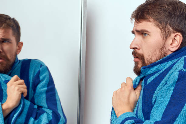 istock a man in a blue robe examines himself in a mirror in a bright room cropped view 2111862678