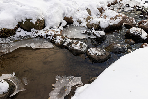 a narrow small river in winter covered with snow and ice, the ice on the river is reinforced with a plastic geogrid