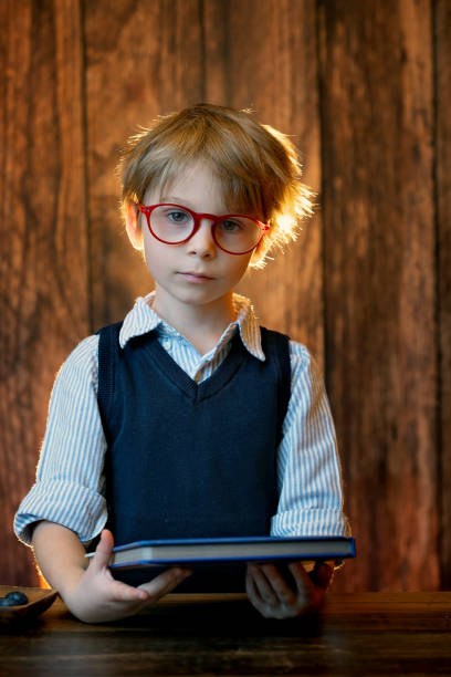 Cute child, boy wearing glasses, reading a book at home, studio shot
