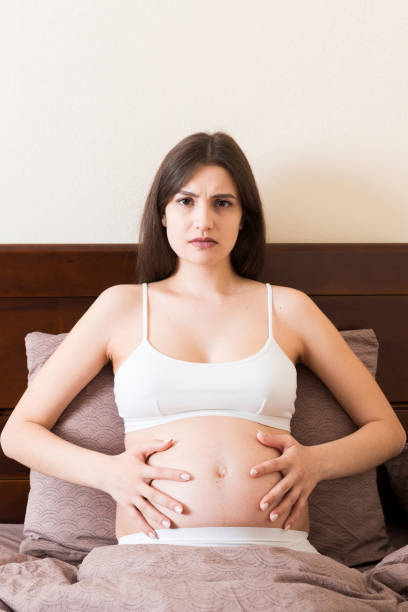 young pretty pregnant woman, in pain, sitting on bed in bedroom, preparing to give a birth - healthcare and medicine bed patience human pregnancy 뉴스 사진 이미지