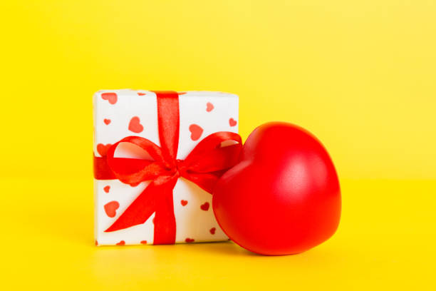 gift box with red bow and red heart on colored background. Perspective view. Flat lay.