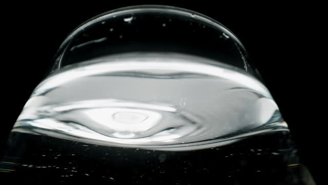 Water droplets dripping into the glass, macro view from a low angle on the silvery surface of the water resembling mercury.
