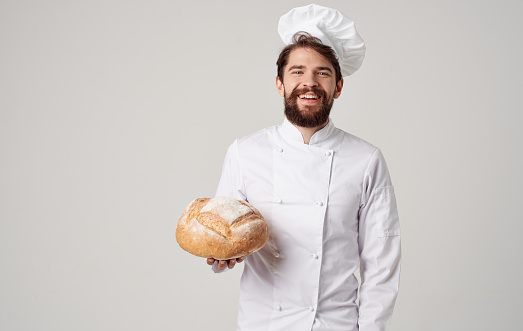 chef with a loaf of bread in his hands on a light background and professional clothing cropped view. High quality photo