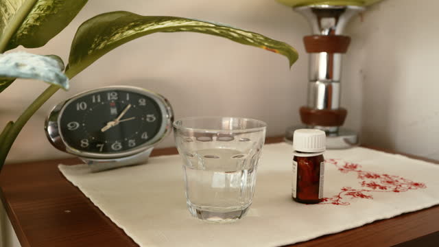 Alarm clock, glass of water and drugs on a bedside table