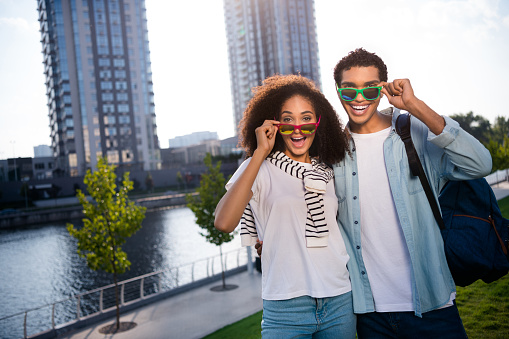 Photo of young happy cheerful positive family couple take off sunglasses looking at cameraman posing like travel tourists outdoors.