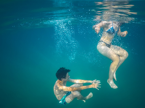 Teenagers wearing swimwear playing under water in the sea, taken with underwater camera